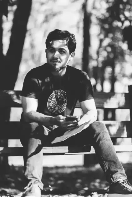 Luiz Sentado em um banco olhando para o lado segurando um celular e uma folha de papel